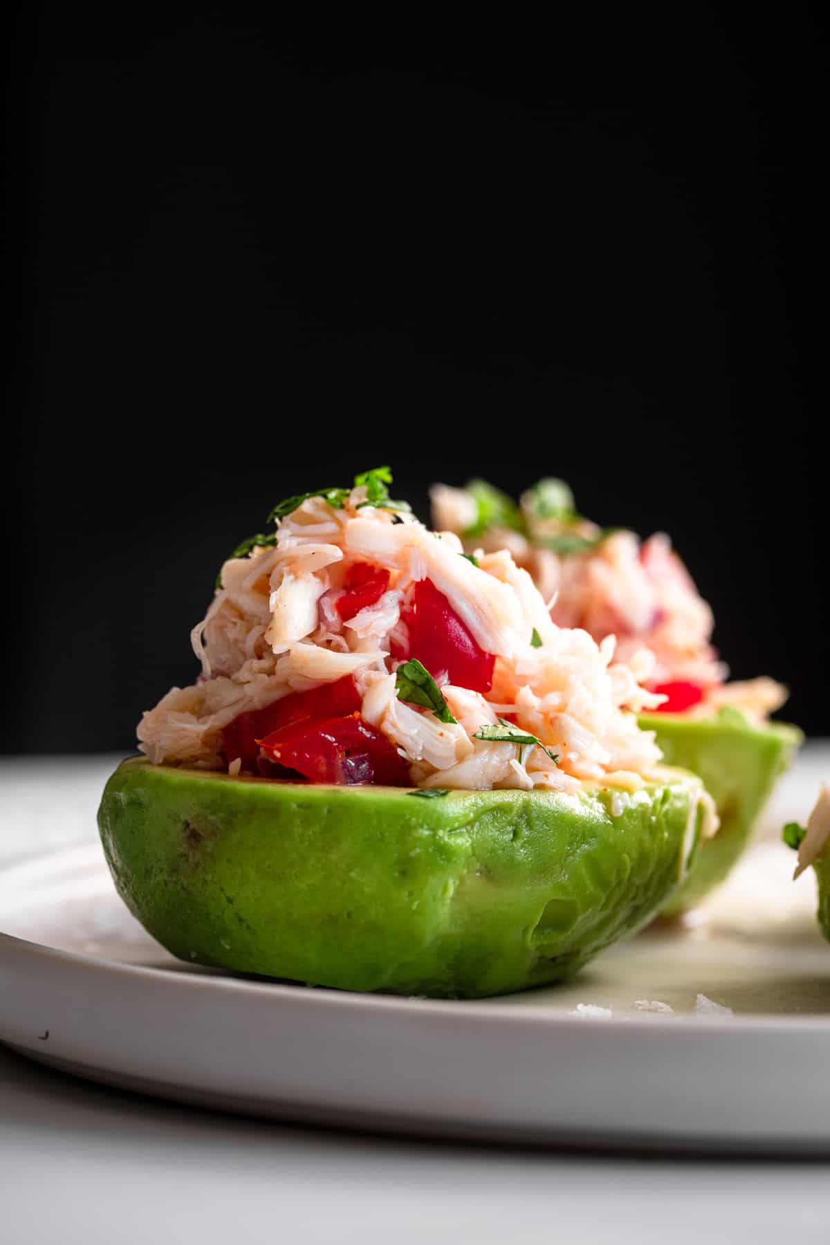 side view close up of avocados with crab salad inside on a black background