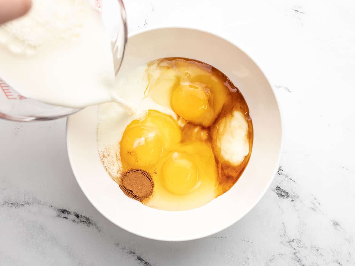 Custard ingredients all added to a white bowl with milk being poured in.