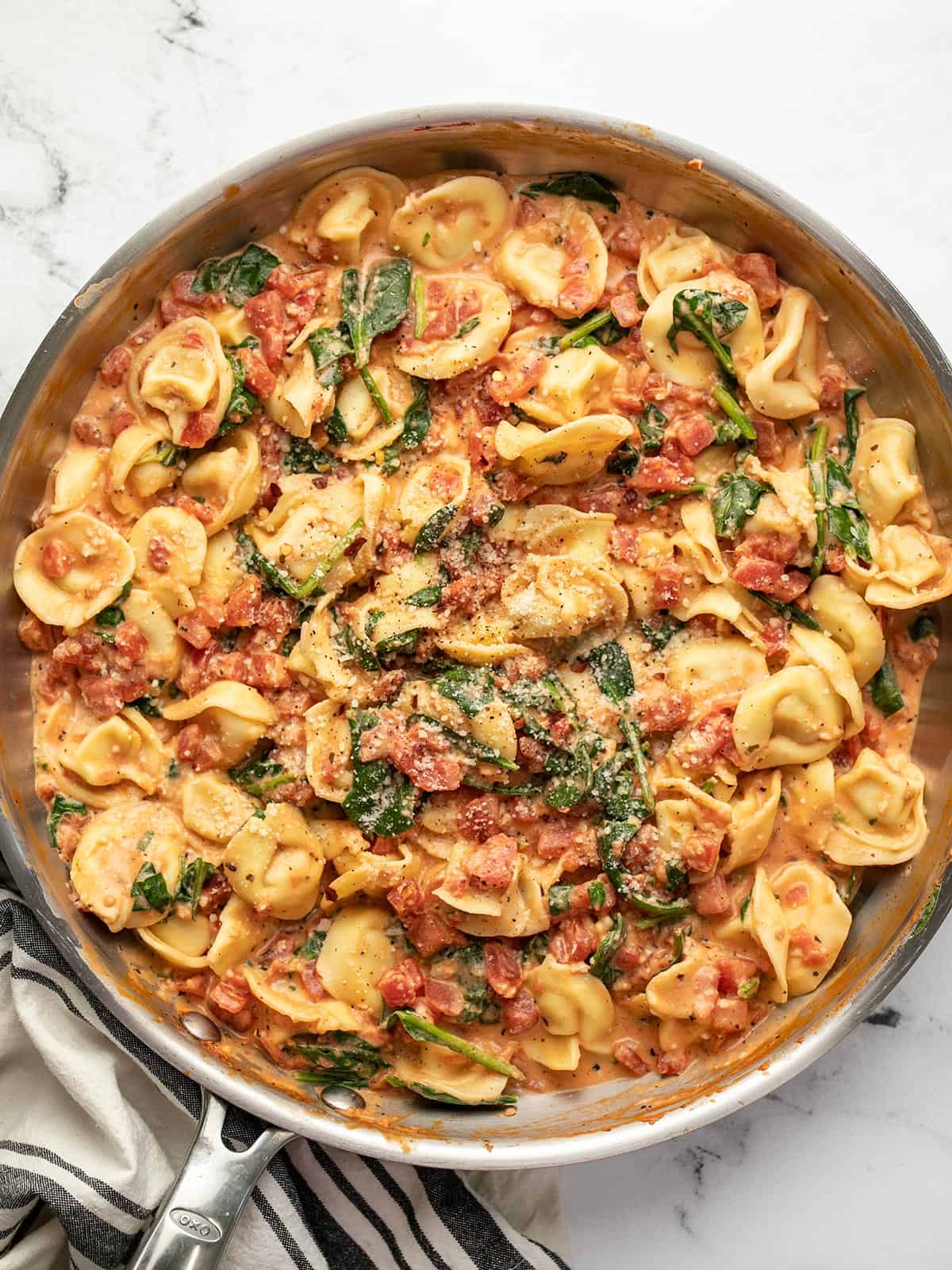 Overhead view of Spinach Tortellini in the skillet garnished with Grated Parmesan.