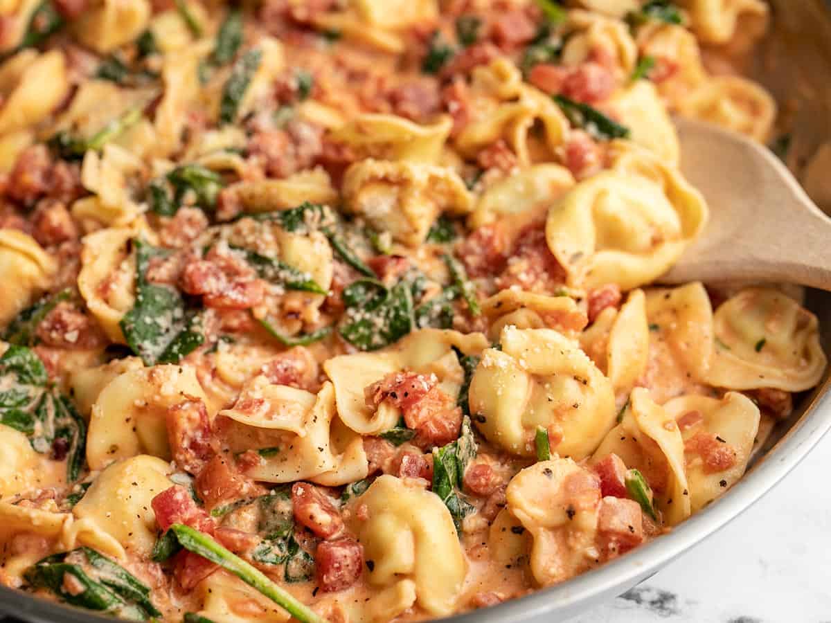 Close up side view of spinach tortellini skillet with a wooden spoon.