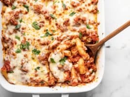 Close up of a wooden spoon in the casserole dish full of baked ziti