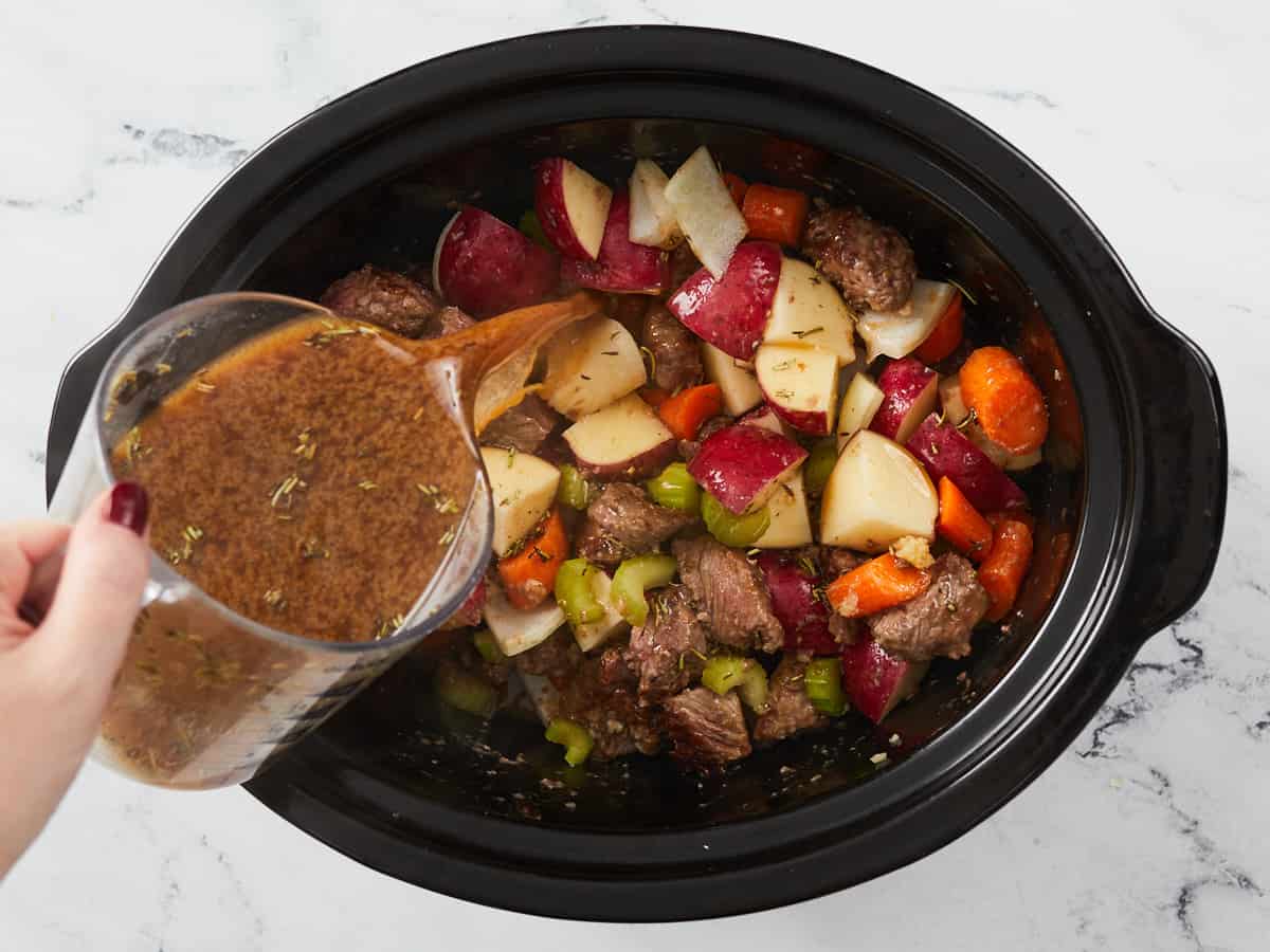 Broth being poured over the ingredients in the slow cooker.