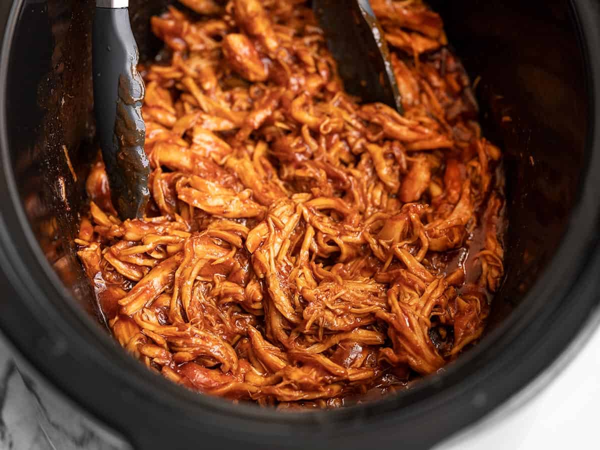 Side view of Slow Cooker BBQ Chicken in the slow cooker with tongs.