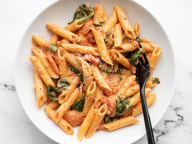 Overhead view of a bowl full of creamy tomato and spinach pasta, a black fork in the side