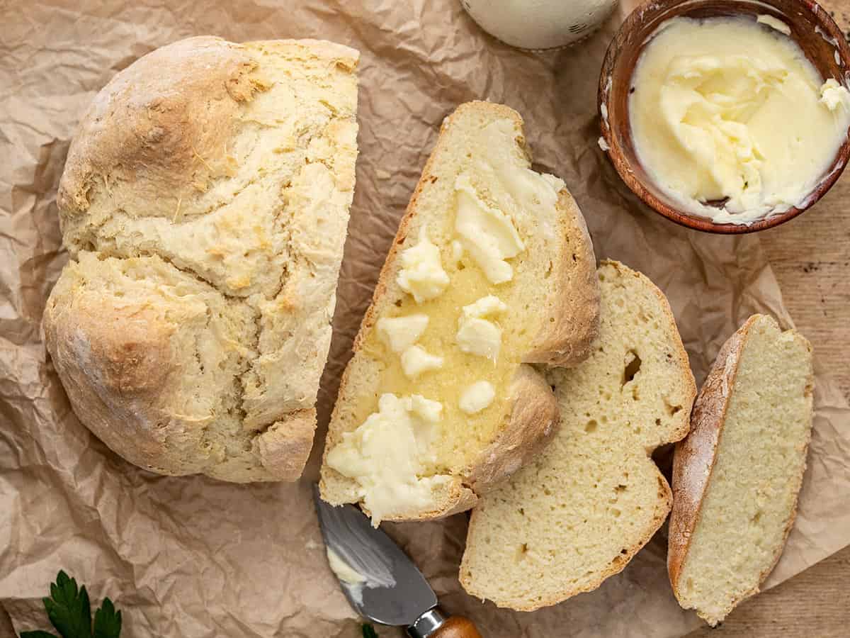 Overhead shot of baked easy soda bread sliced and buttered on parchment.