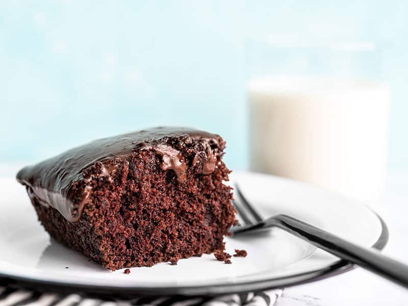 One slice of chocolate depression cake or "crazy cake" viewed from the side, a glass of milk in the background