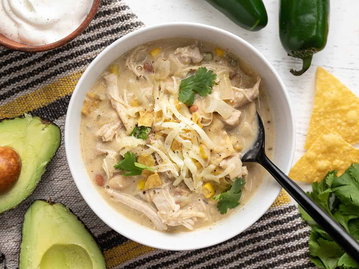 Overhead view of a bowl of creamy white chicken chili with toppings and a spoon.