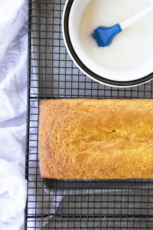 Glazing a French Grandma Lemon Yogurt Cake on a black cooling rack over a pan.