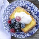 French Grandma lemon yogurt cake with berries, powdered sugar, and yogurt on a blue and white plate with a white linen.