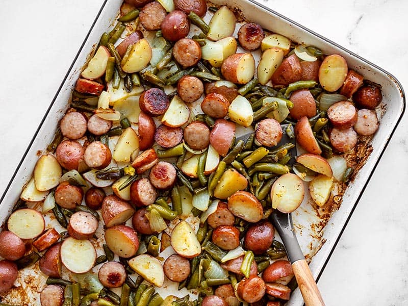 Sheet pan roasted kielbasa potatoes and green beans with a spatula