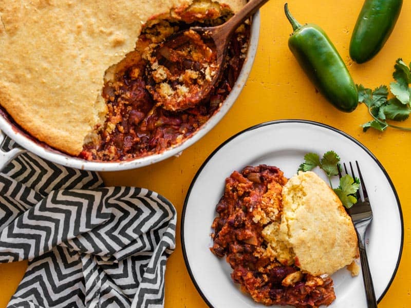 Chili cornbread skillet with some scooped out onto a white plate beside the skillet