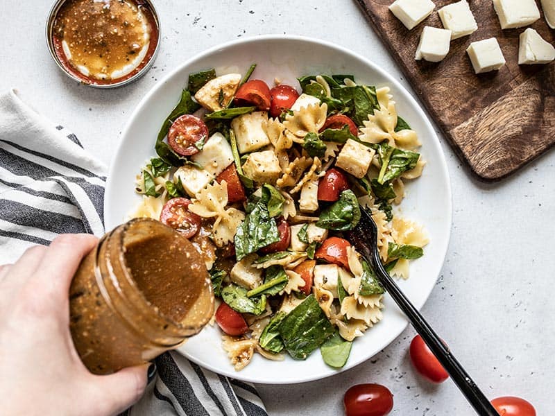 Parmesan Balsamic Vinaigrette being poured onto a bowl of Tomato Mozzarella Salad from a jar.