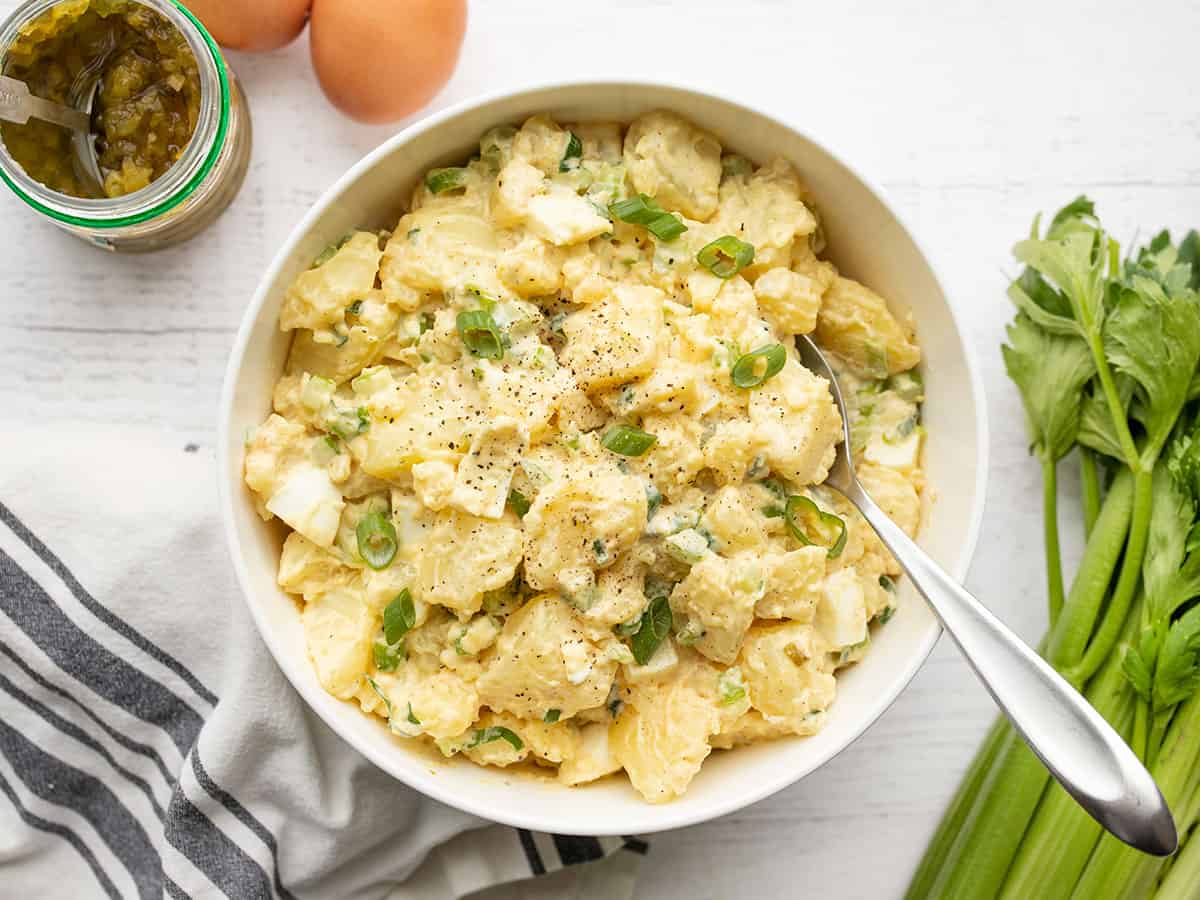 overhead view of a a bowl full of potato salad with celery, relish and eggs on the sides