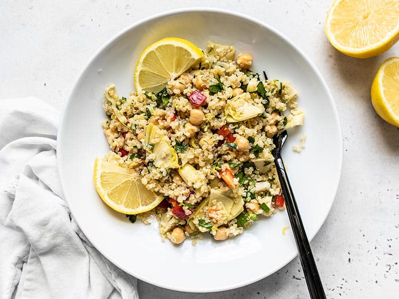 Overhead view of Lemony Artichoke and Quinoa Salad in a bowl with lemon wedges and a fork.