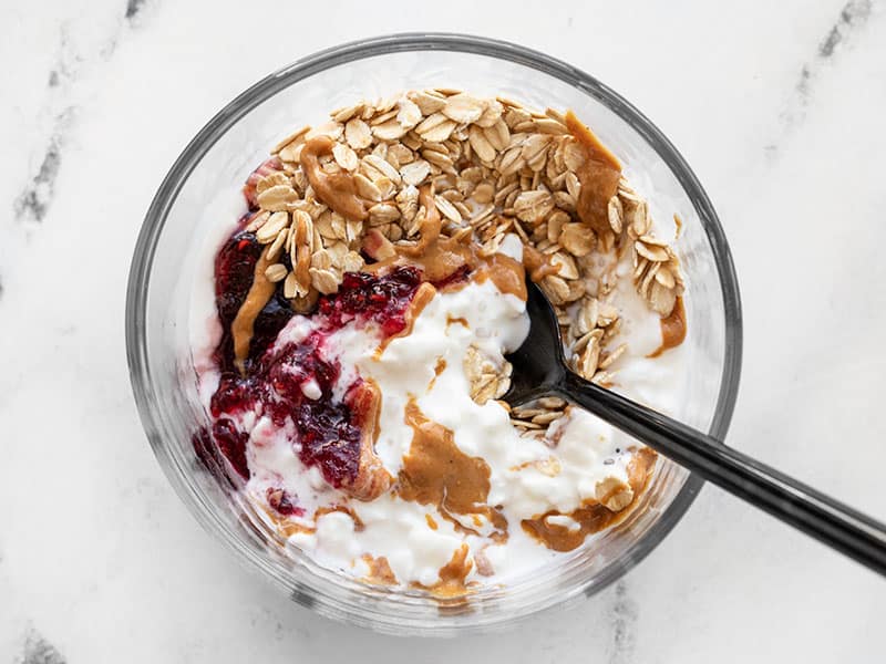 A spoon digging into a glass container full of a Peanut Butter and Jelly Cottage Cheese Breakfast Bowl