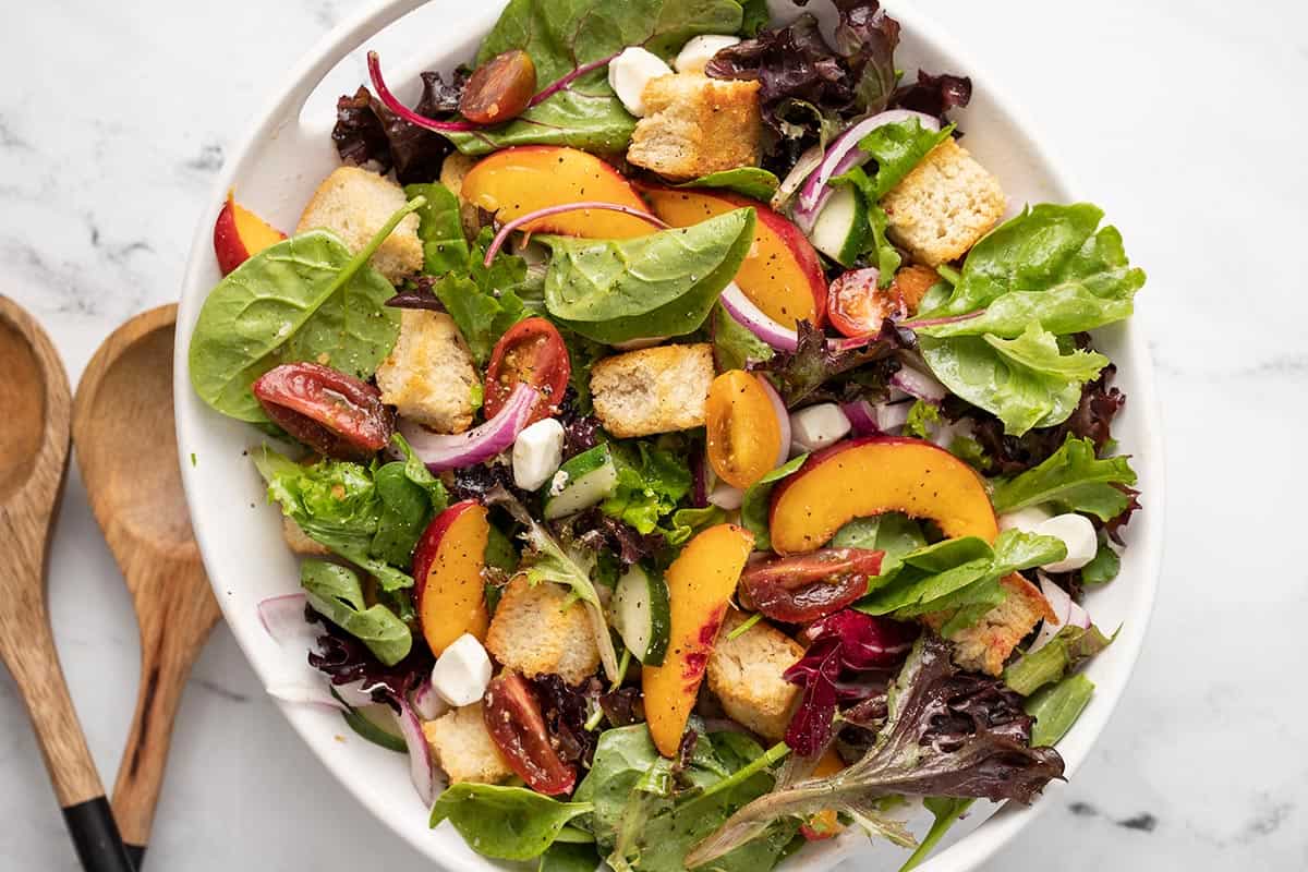 Overhead shot of panzanella salad in a white bowl with wood serving spoons next to it.