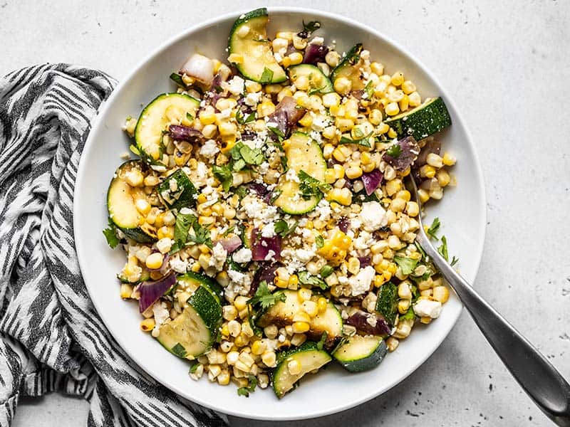 Overhead view of a bowl of Charred Corn and Zucchini Salad with a black and white napkin on the side.