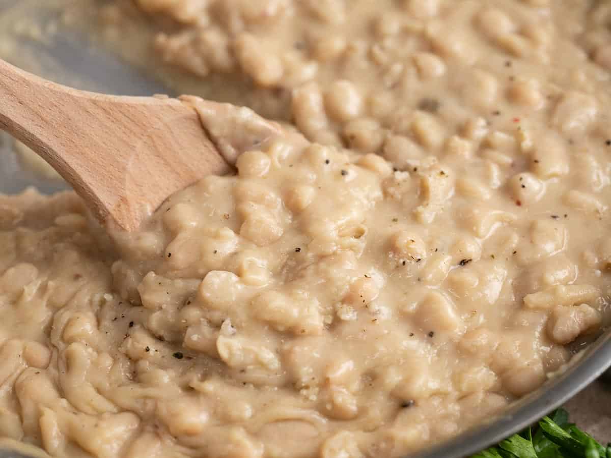 Close up side view of a wooden spoon stirring Parmesan Beans.