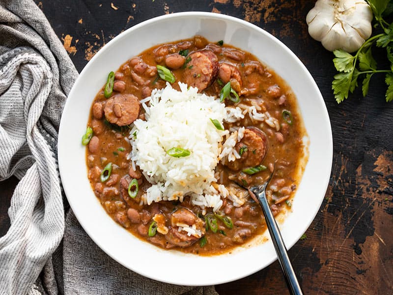 A bowl full of red beans and rice with sausage, a spoon in the center of the bowl