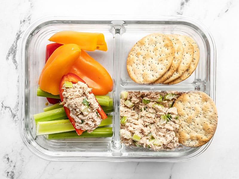 A tuna salad lunch box with tuna in a pepper and a cracker tipping into the salad