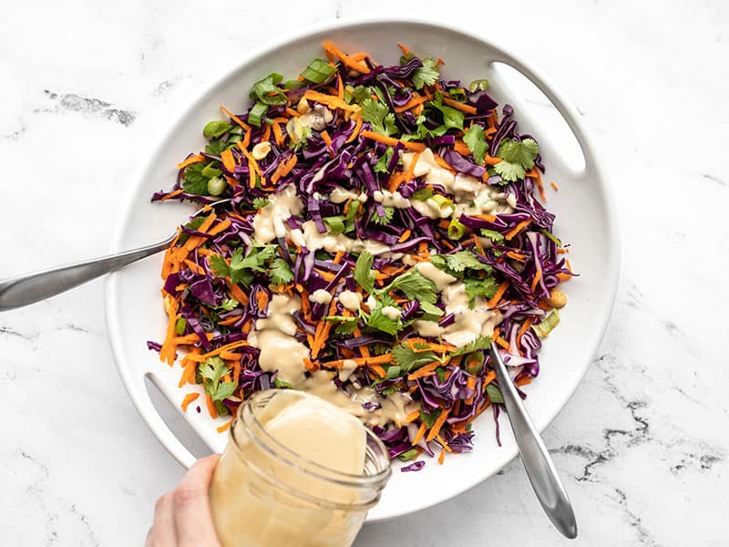 Sesame ginger dressing being poured over the crunchy cabbage salad