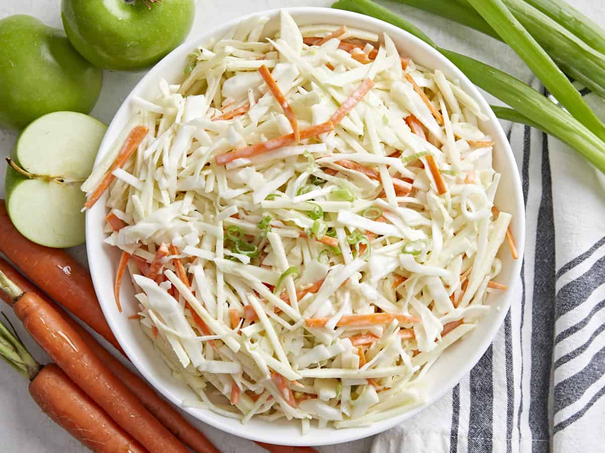 Overhead view of a bowl full of apple slaw with the ingredients on the sides.