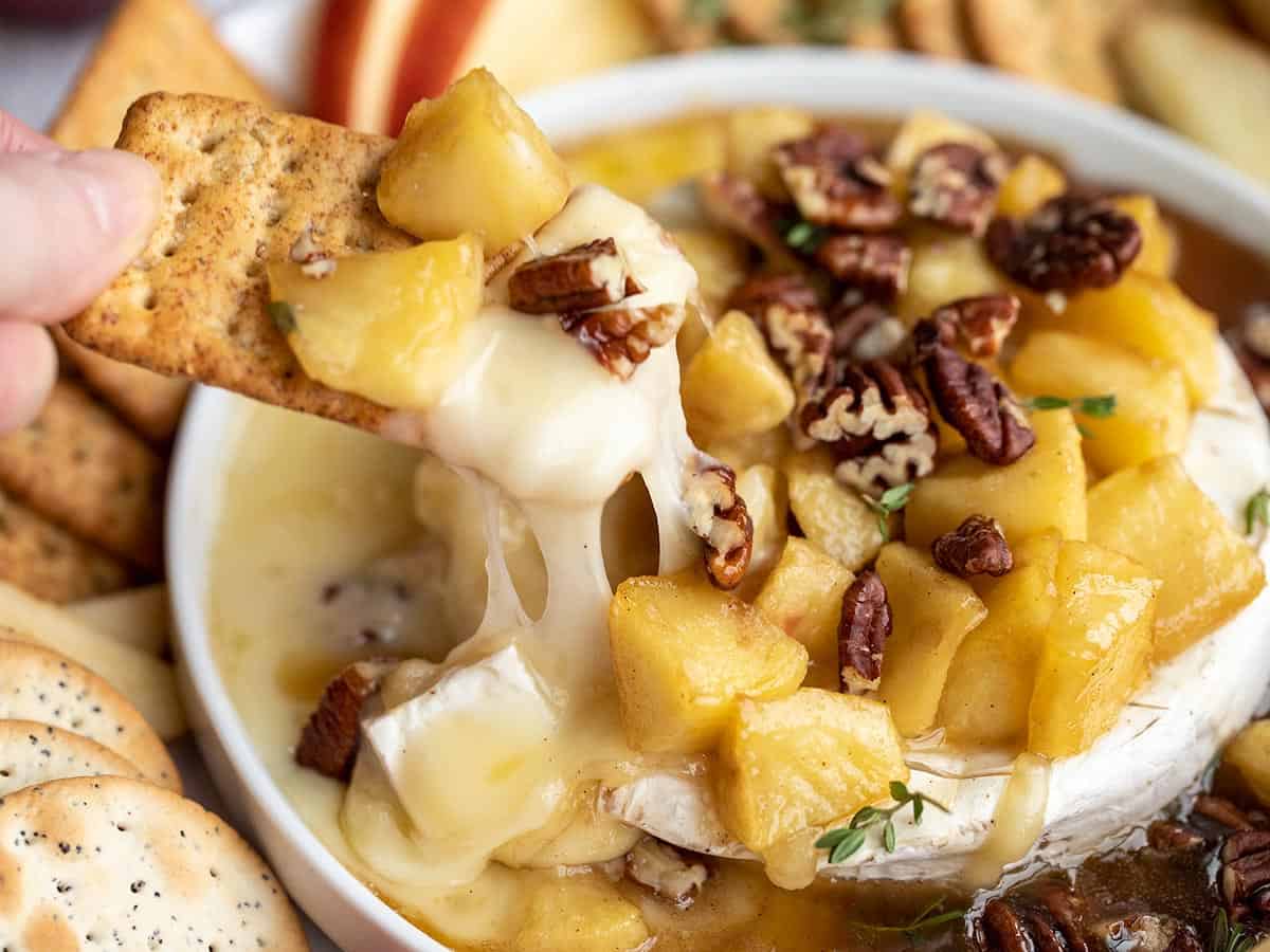 close up of a cracker dipping into the baked brie with cheese pull