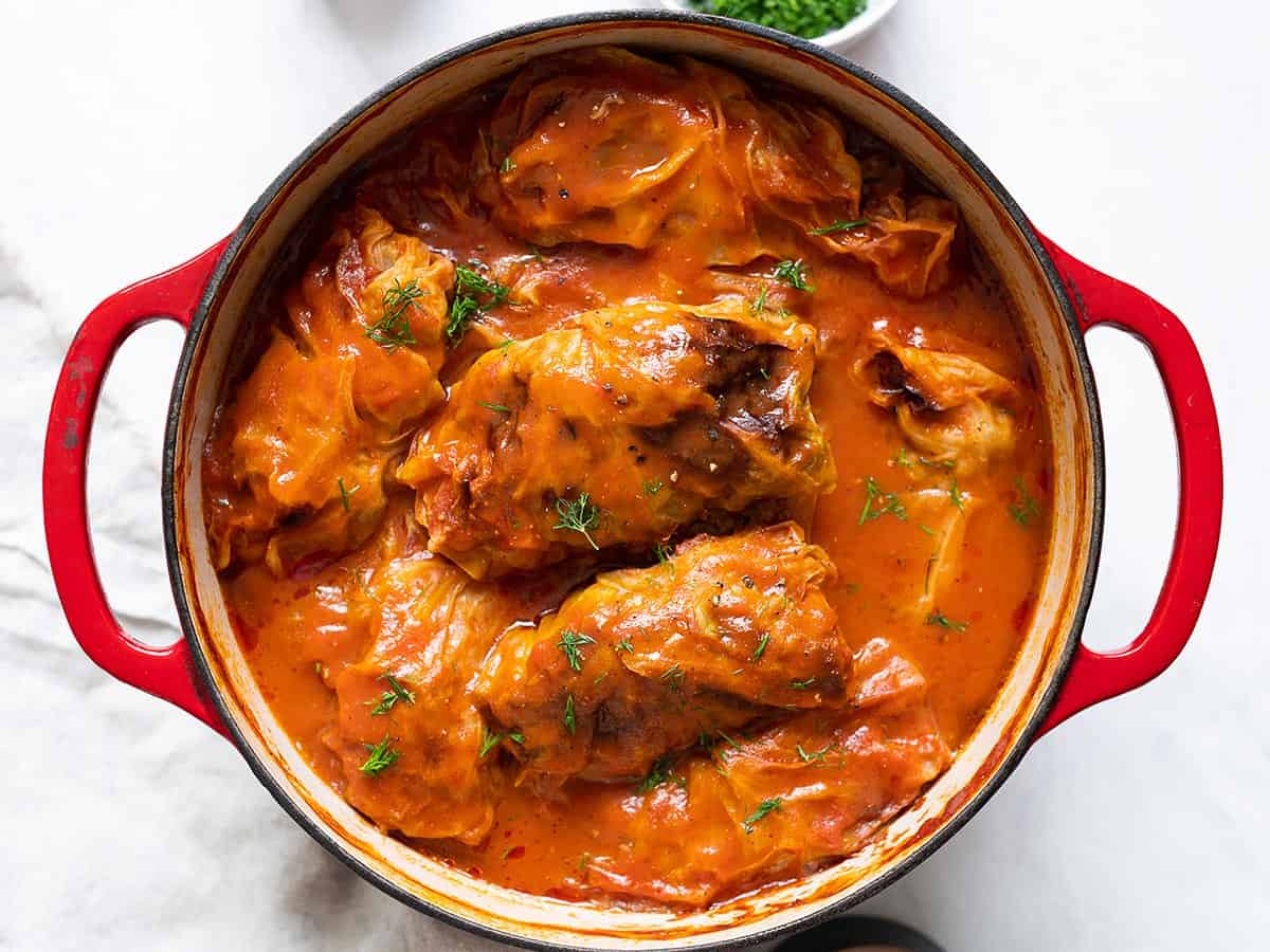 overhead view of cabbage rolls in a stock pot with tomato sauce poured on top and garnished with fresh dill