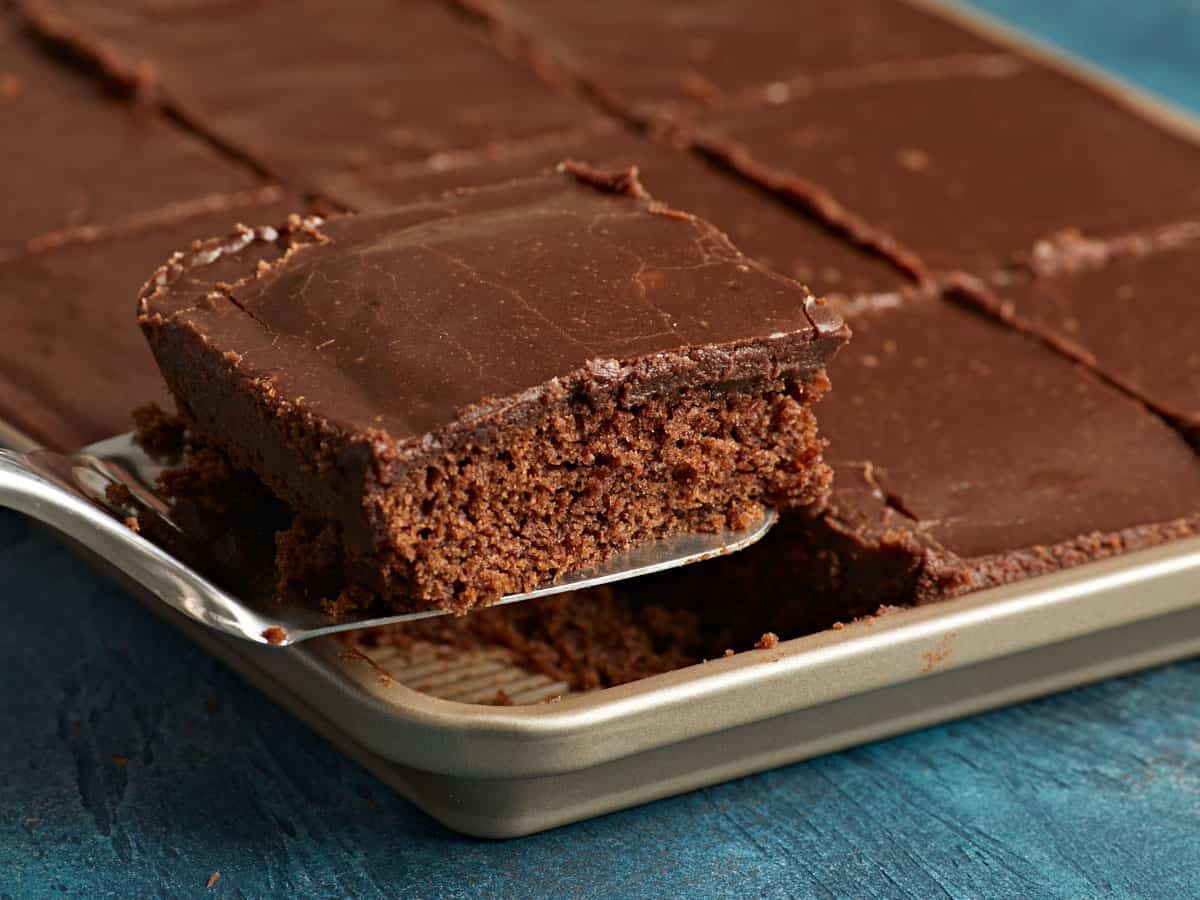 A slice of chocolate cake being lifted out of the sheet pan.