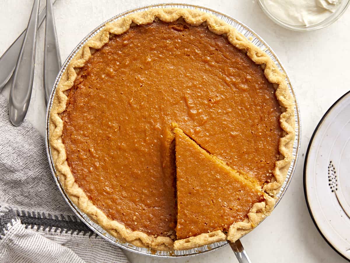 Overhead view of a whole sweet potato pie with one slice cut and being lifted out of the pie pan.