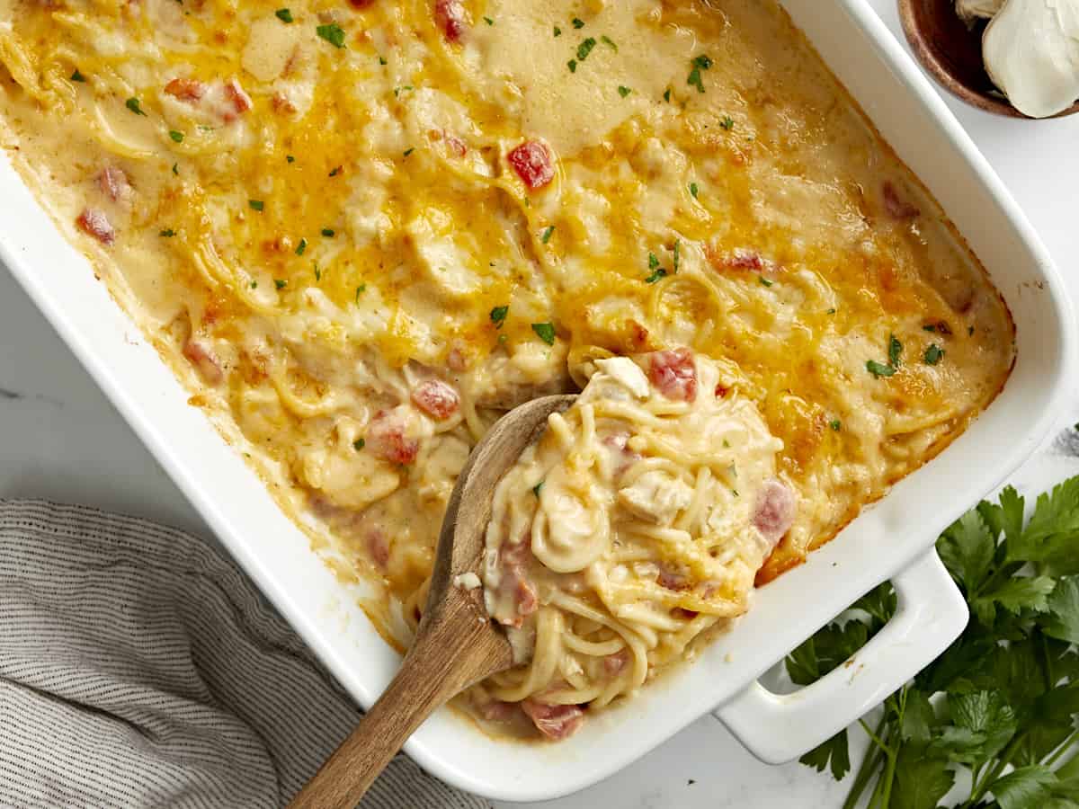 Overhead view of chicken spaghetti in a white casserole dish with a wooden spoon placed inside.