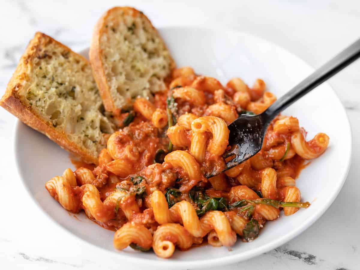 front view of a bowl full of creamy tomato pasta with sausage, a bit lifted on the fork