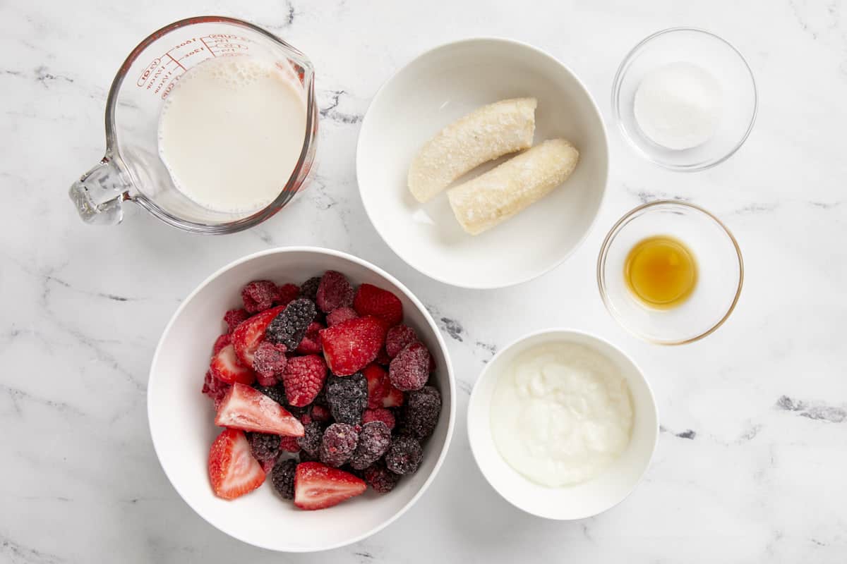 Overhead shot of mixed berry smoothie ingredients separated in different bowls.