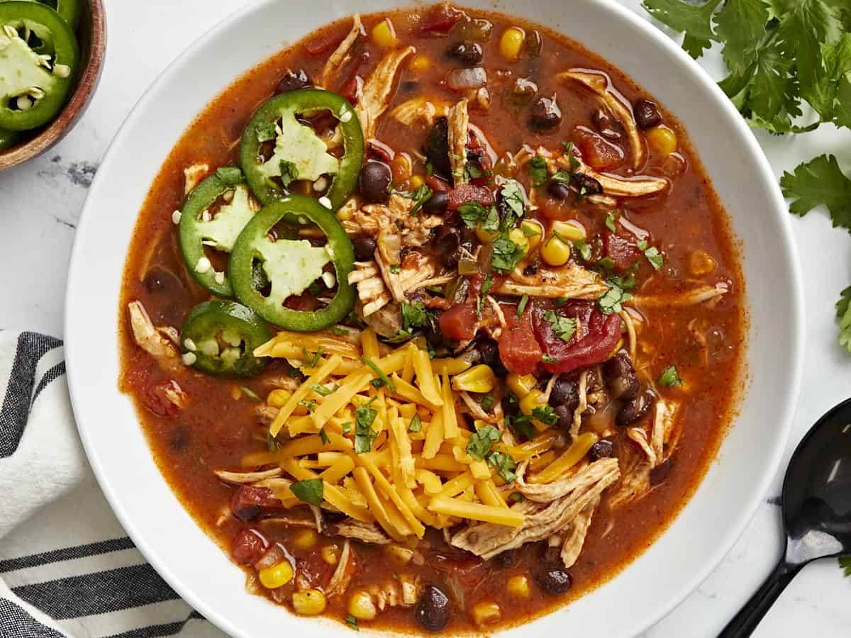 Overhead view of Chicken Enchilada Soup in a white bowl with a black spoon on the side.