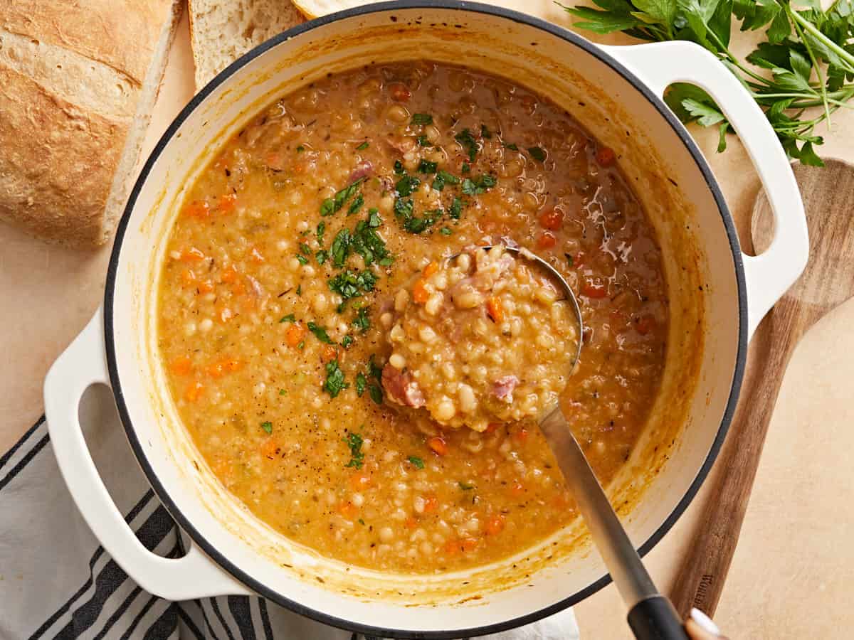 Overhead view of a dutch oven pot full of navy bean soup with a ladle scooping some out.