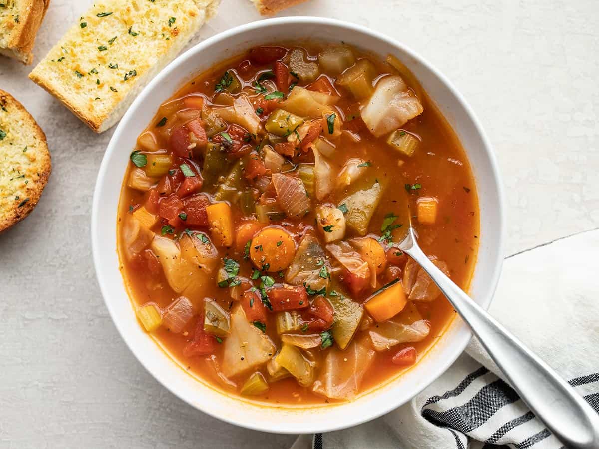 a bowl of cabbage soup with a spoon and garlic bread on the side