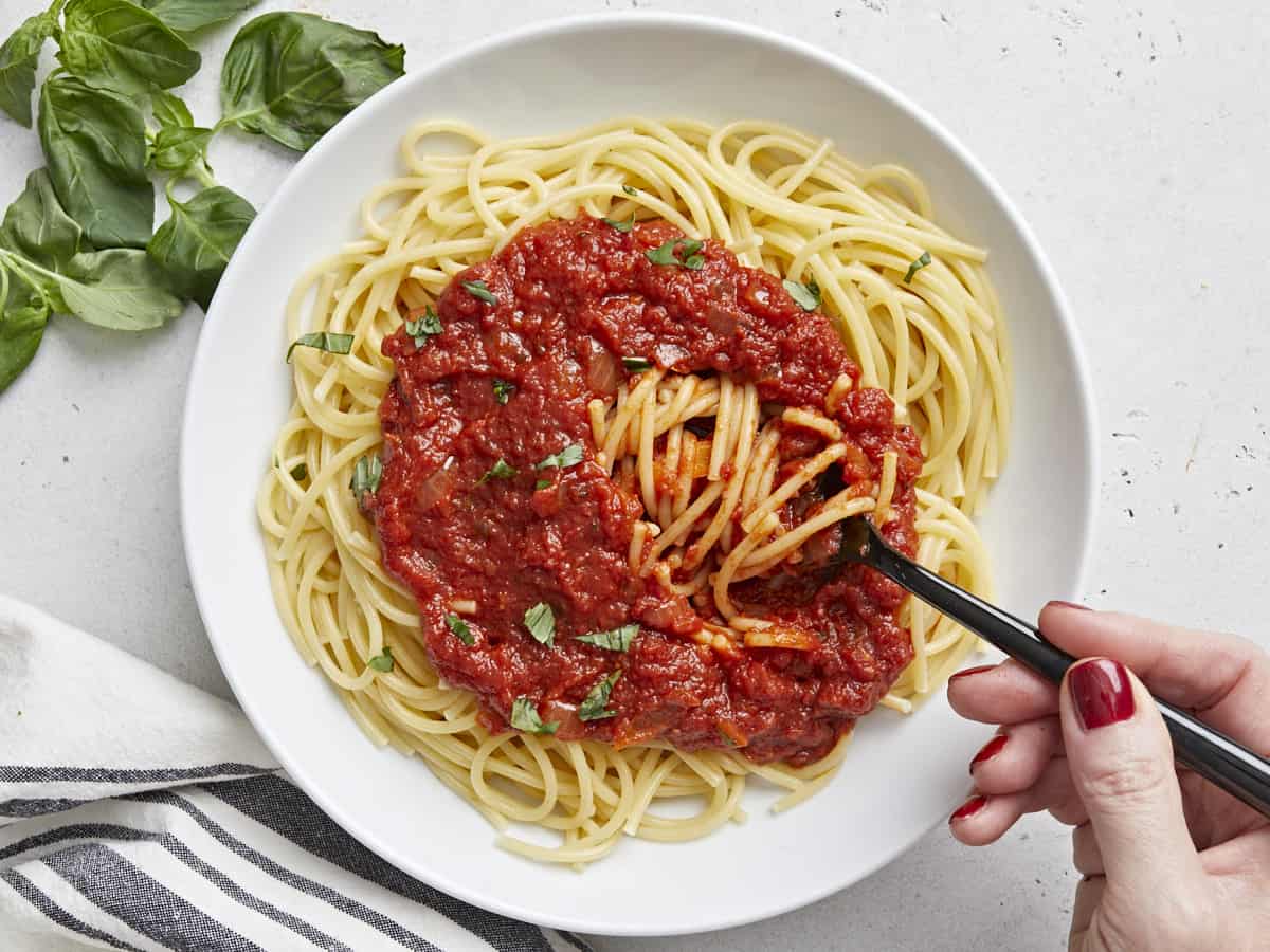 A fork twirling into a pile of pasta covered in marinara sauce.