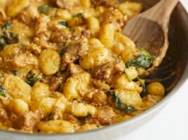 Side shot of Creamy Chicken and Gnocchi in a silver skillet with a wooden spoon in it.