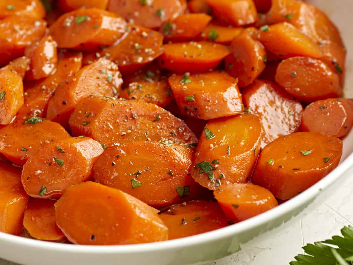 Side close up view of glazed carrots in a serving dish and garnished with parsley.