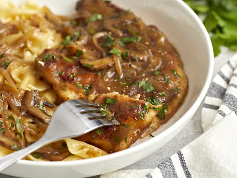 a fork holding a piece of chicken marsala above a shallow dish.